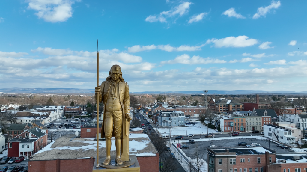 Drone photography example: A close up on a statue at the top of a building with a city behind it