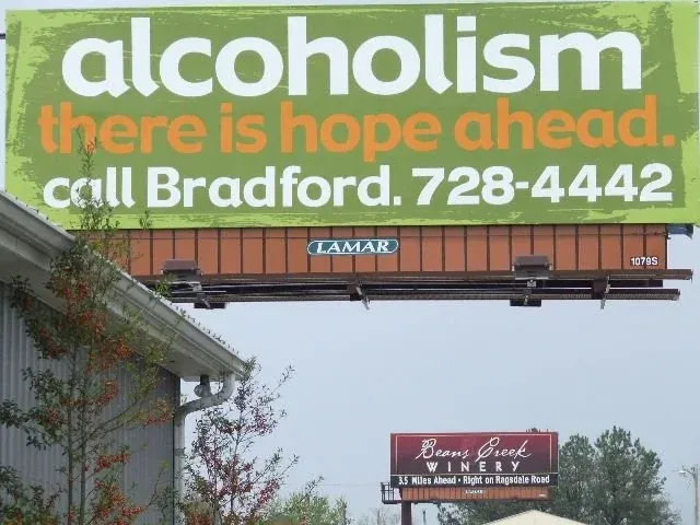 A billboard that says "Alcoholism: there is hope ahead" with a winery's billboard just in the background