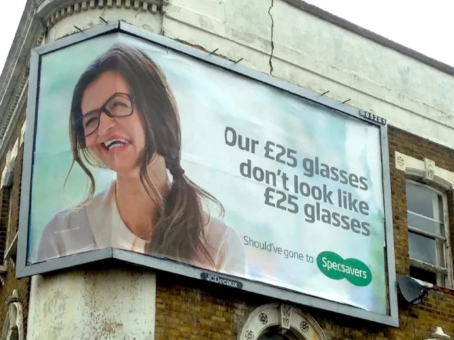 A billboard that's been stretched to fit over a corner, distorting the picture of the woman and the glasses she is modeling