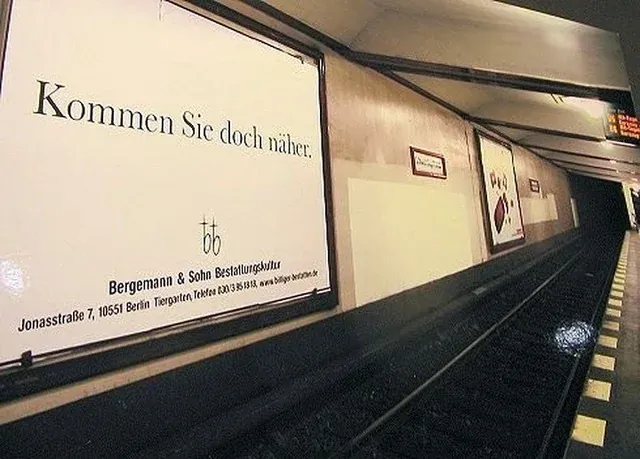 A poster hanging over train tracks that says, "Kommen Sie doch näher."